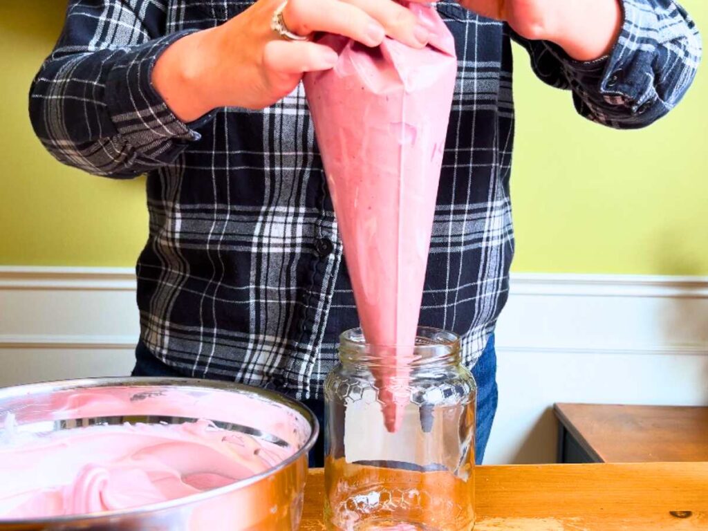 A woman is holding a piping bag full of pink coloured French meringue.