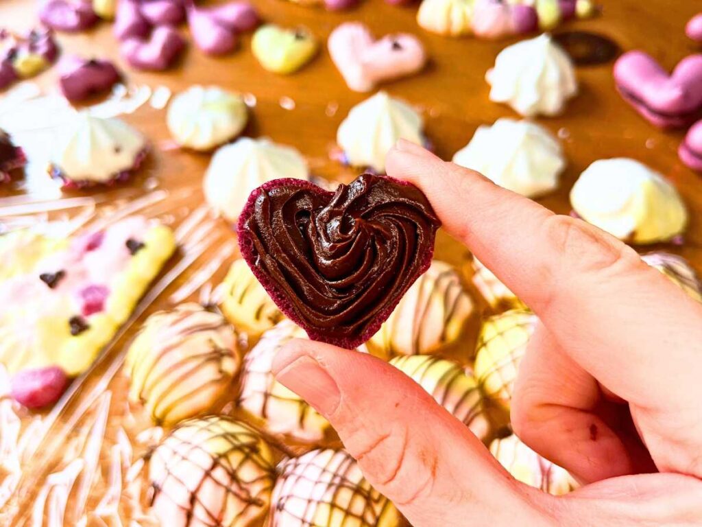 A woman is holding a heart meringue with chocolate ganache.