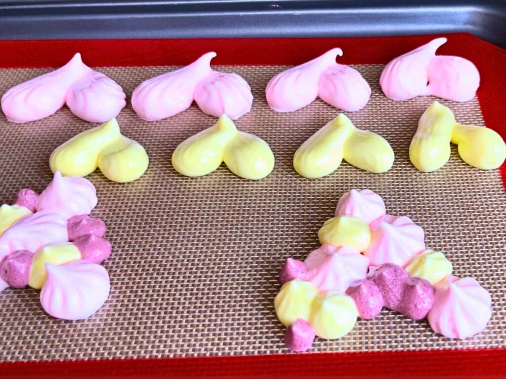 Piped heart shaped meringues on a lined baking sheet.