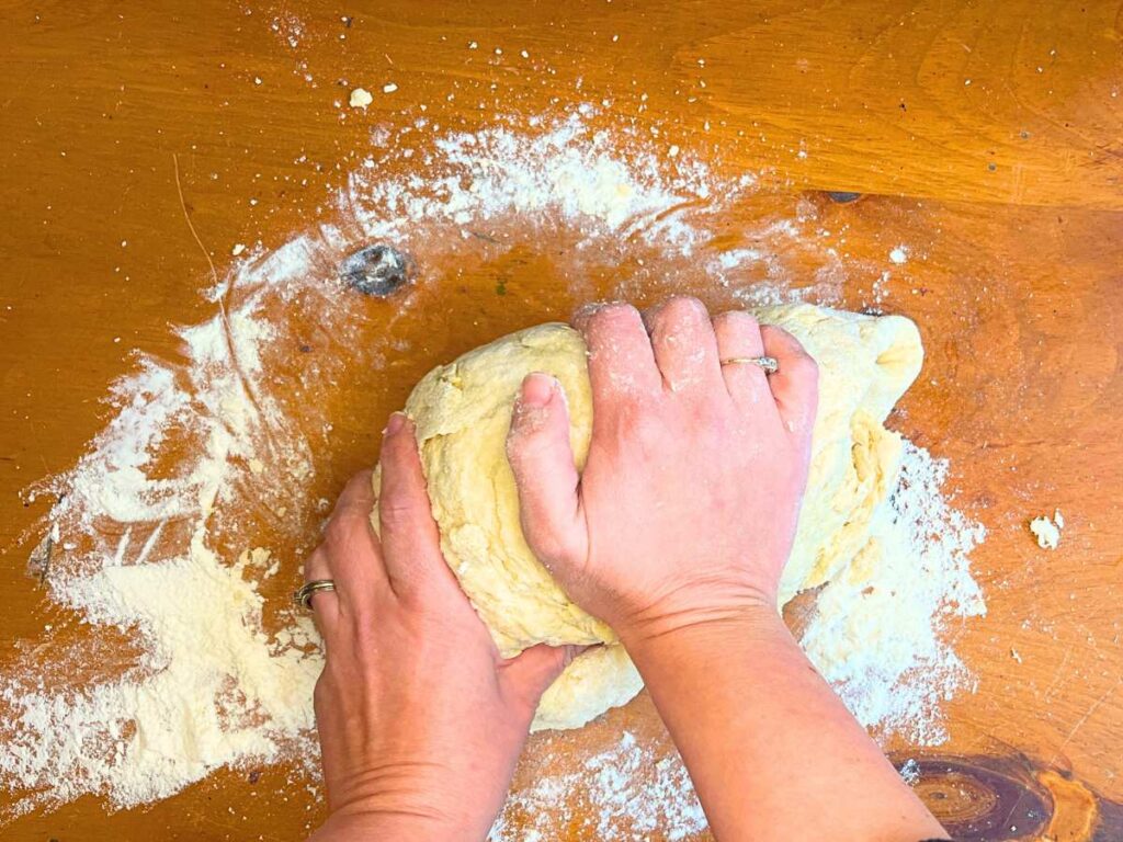 A woman is kneading cornmeal bread dough on a wooden table.