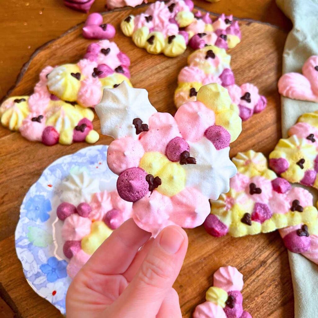 A woman is holding a multicoloured heart shaped meringue cookie.