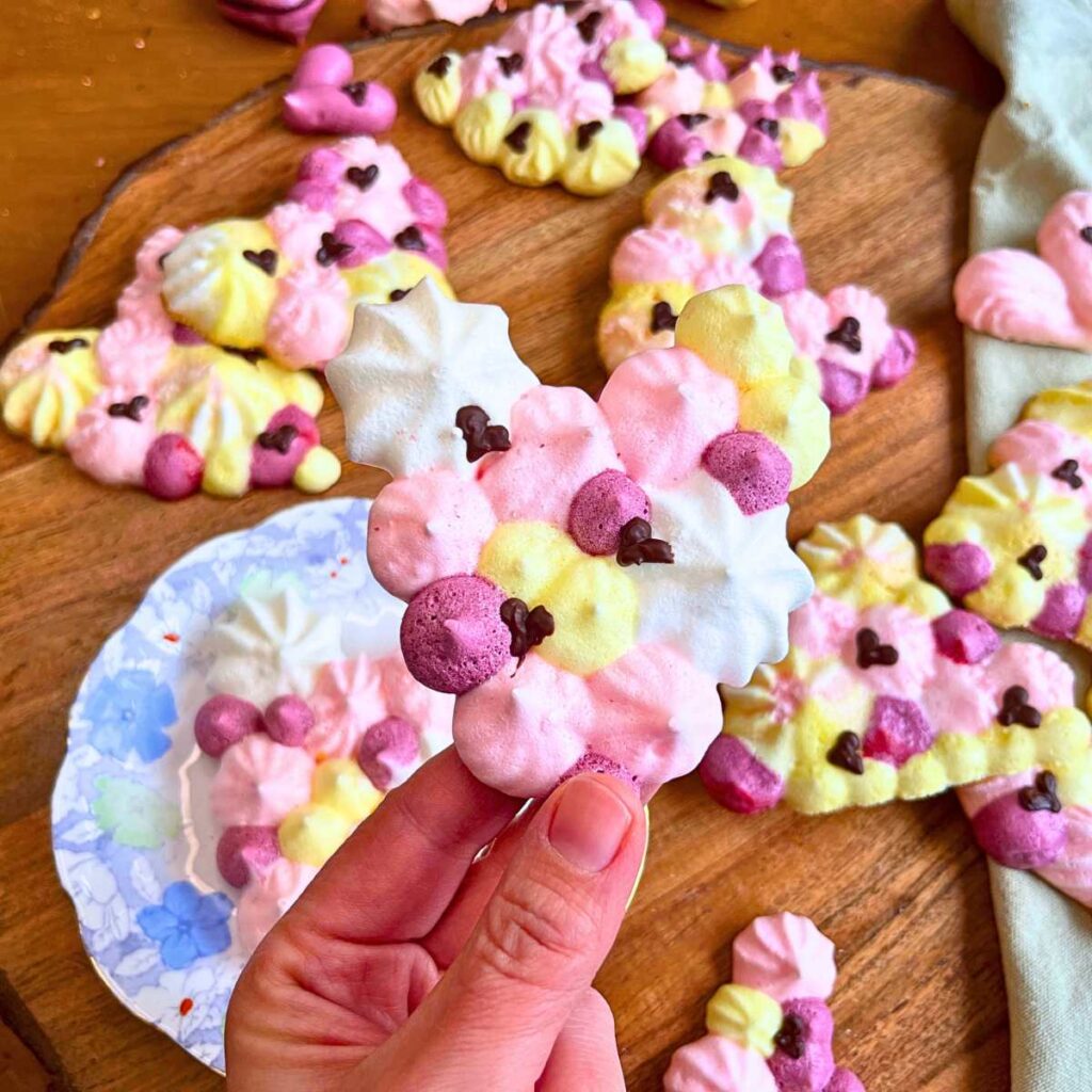 Different coloured heart shaped meringue cookies with some chocolate heart designs on top. A woman is holding one of the heart shaped cookies.