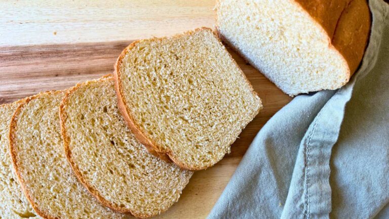 A sliced loaf of white cornmeal sandwich bread on a wooden cutting board.