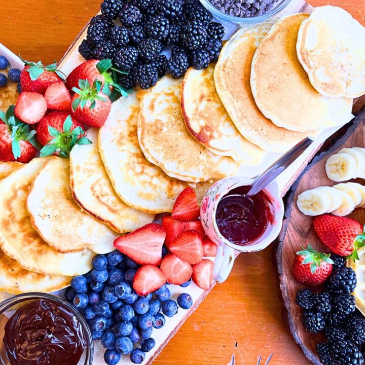 A board with pancakes, fresh fruit, and sauces.