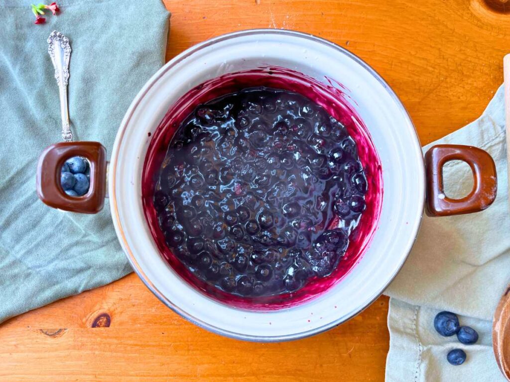 A white sauce pot with cooked blueberry sauce inside.