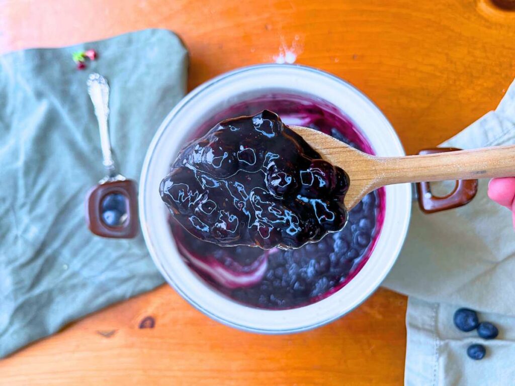 A woman is holding a wooden spoon full of blueberry sauce.