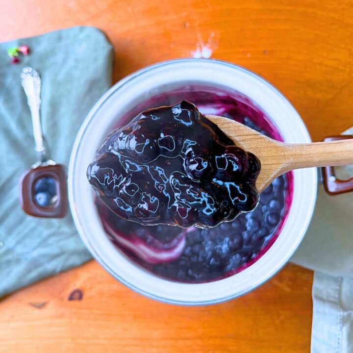 A woman is holding a wooden spoon full of blueberry sauce.