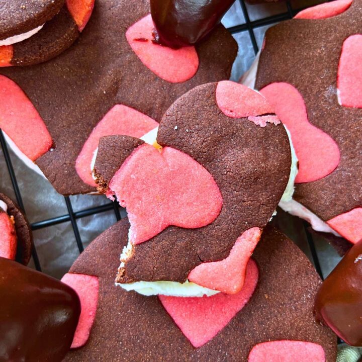 A heart shaped two-tone chocolate and strawberry sandwich cookie. There is a bite out of it.