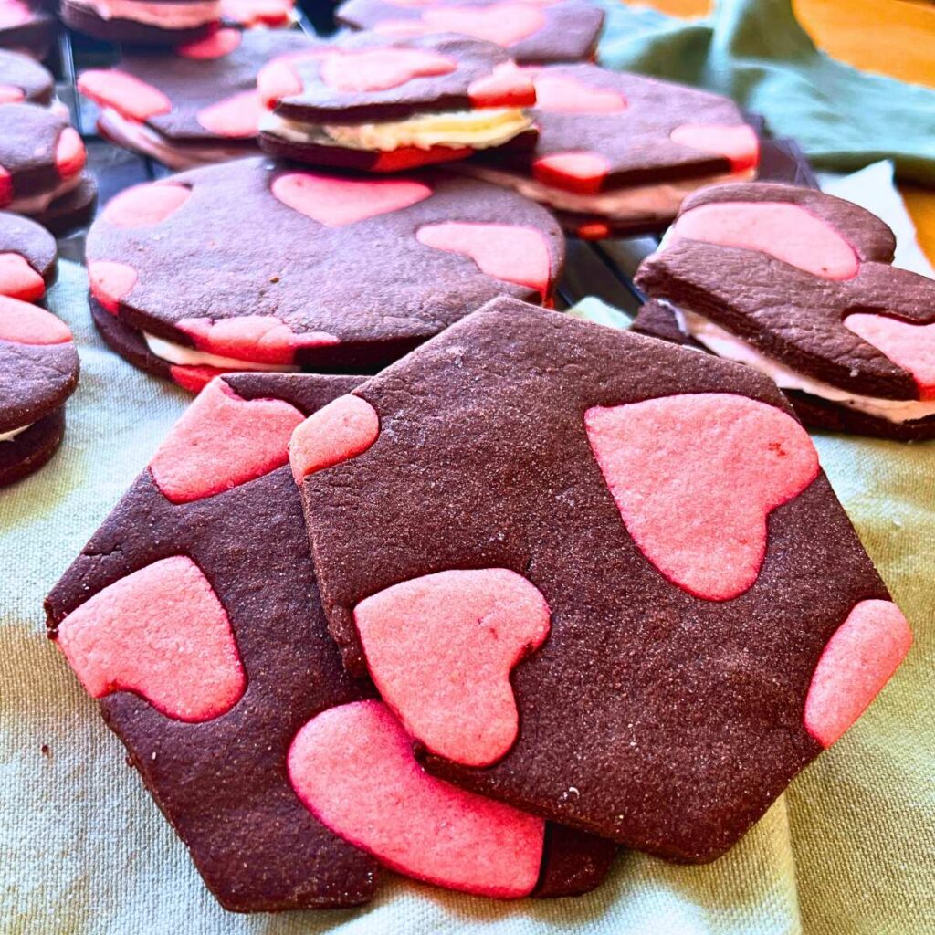 A stack of strawberry and chocolate two-tone cookies. There are more sandwiched in the background.