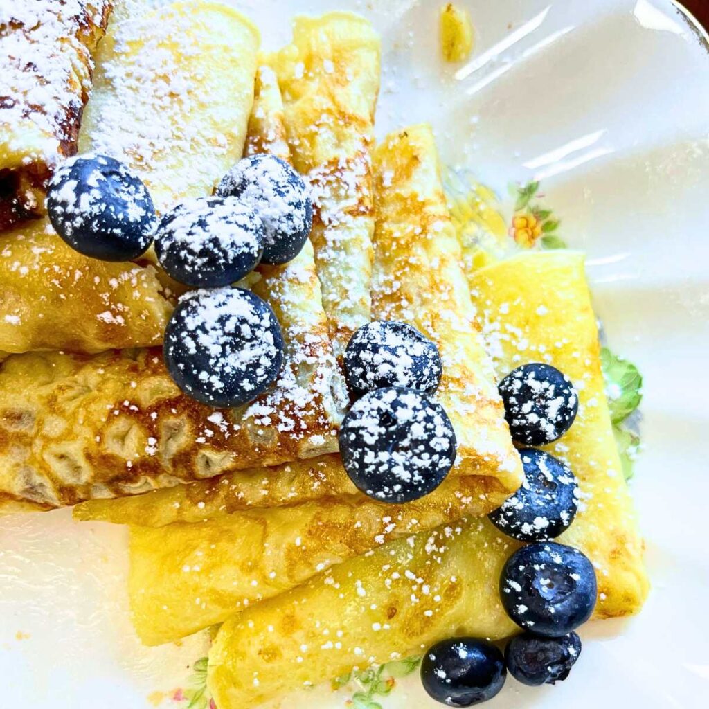 A platter of folded crepes with blueberries and powdered sugar on top.