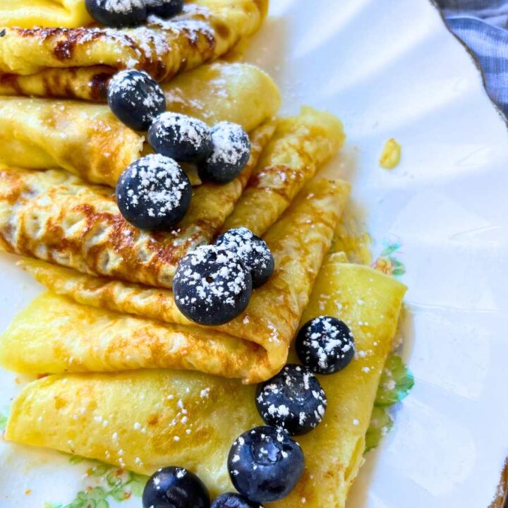 A plater of folded crêpes. There are blueberries and powdered sugar on top.