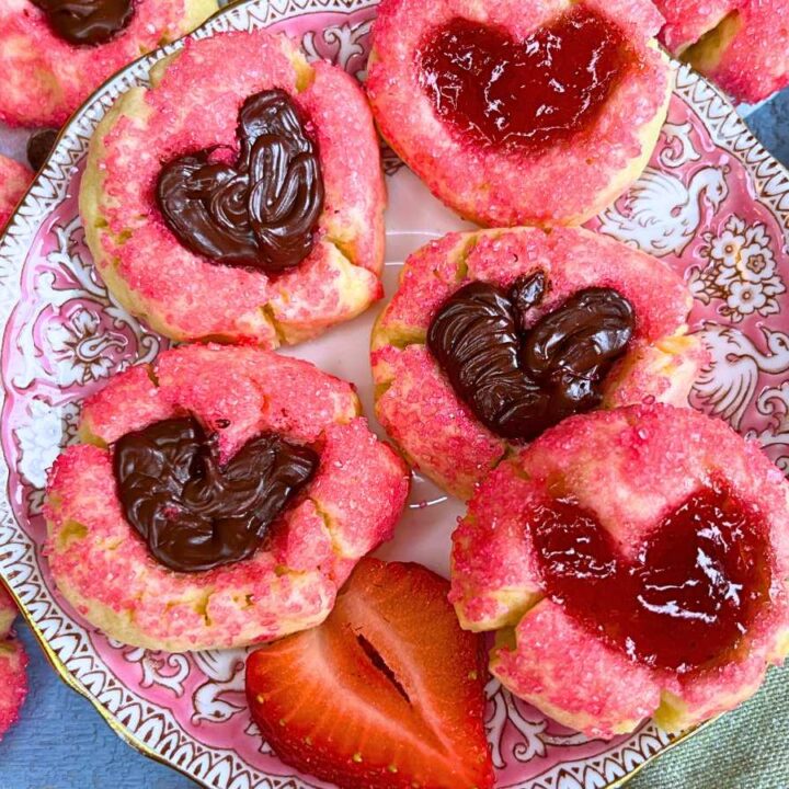 A pink plate full of thumbprint cookies coated in pink sugar. The heart shaped depression is filled with jam and chocolate.