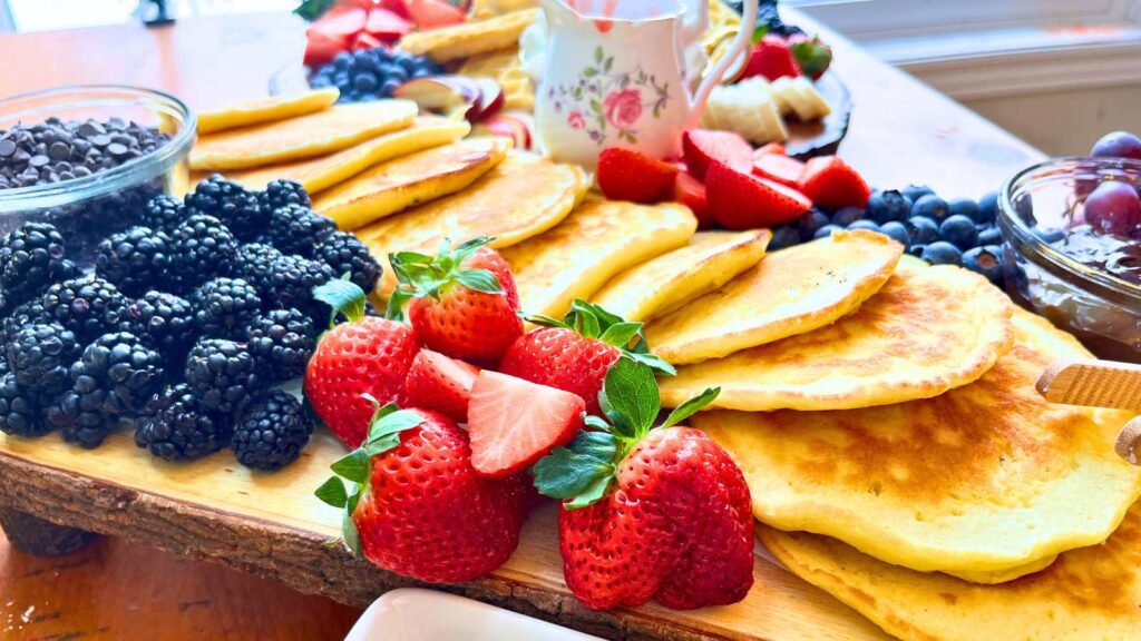 A row of pancakes on a wooden board surrounded by fresh fruit.