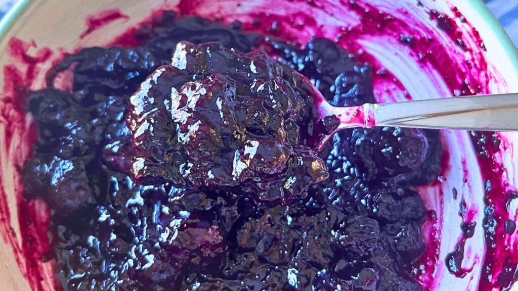 A woman is scooping up blueberry sauce with a metal spoon.