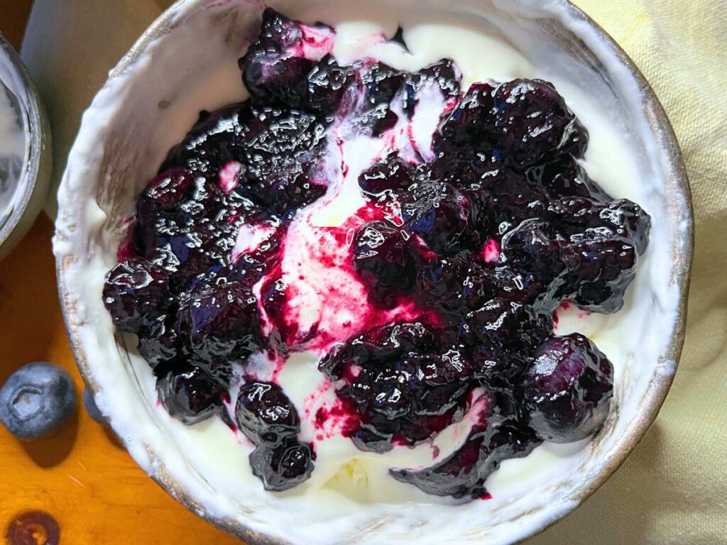 A bowl of vanilla ice cream in a metal bowl. There is blueberry sauce on top.