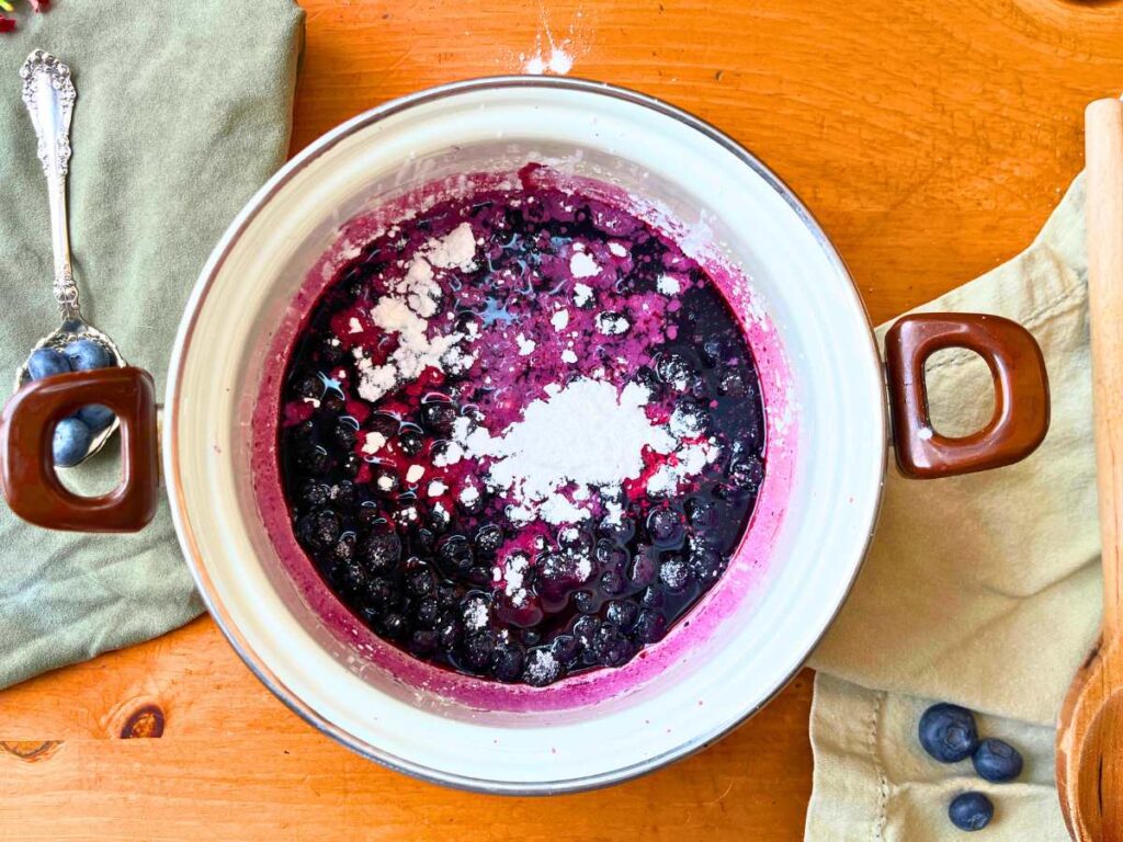 A white sauce pot with cooked blueberries and cornstarch inside.