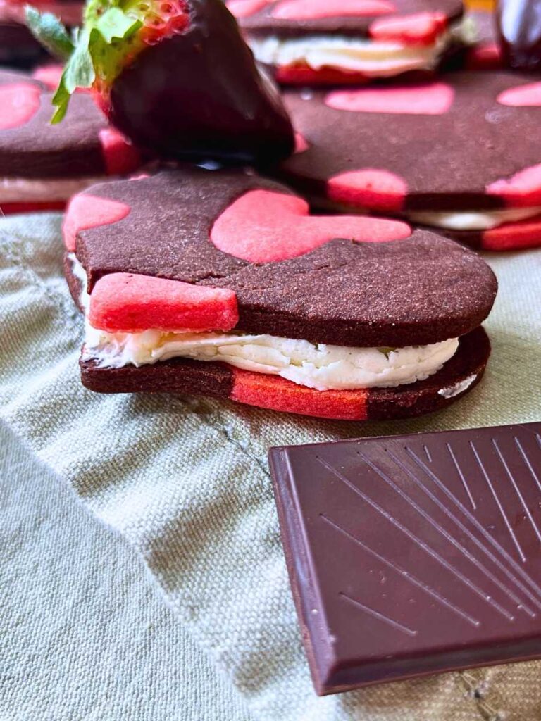 A side view of a heart sandwich cookie, showing the strawberry icing.