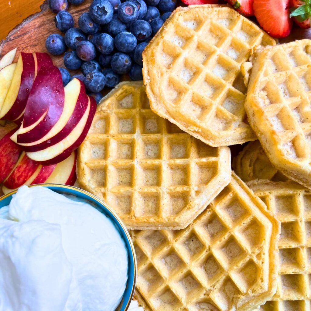 A board with waffles surrounded by fresh fruit and whipped cream.