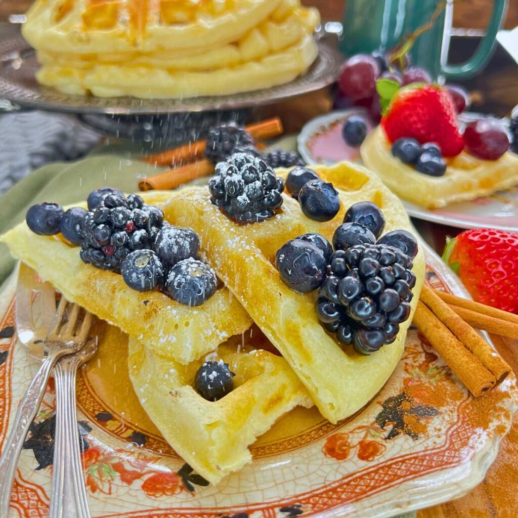 A plate of waffles topped with blueberries and blackberries. There are more waffles in the background.