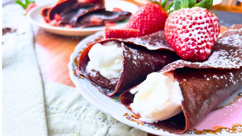 Two chocolate crêpes rolled in cream. There are strawberries on top.