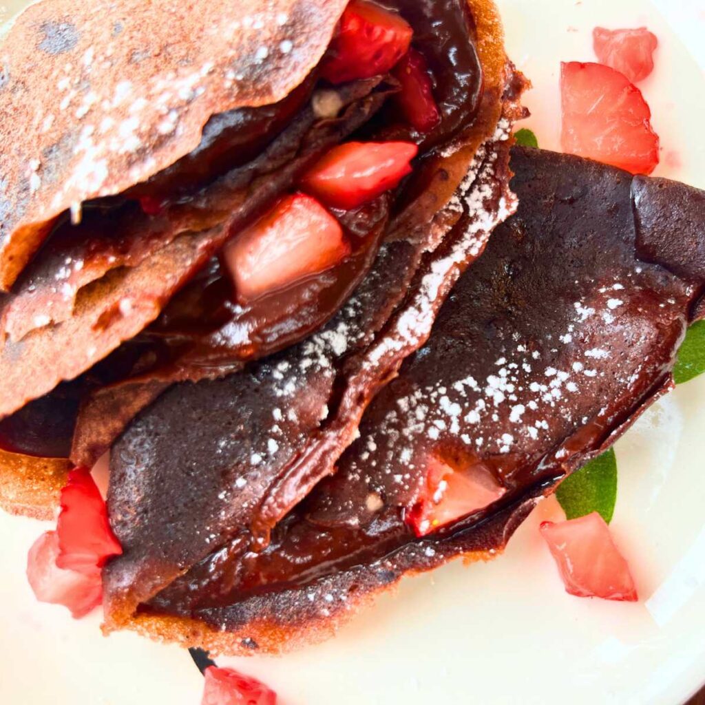 Two folded chocolate crêpes with chocolate and strawberries inside.