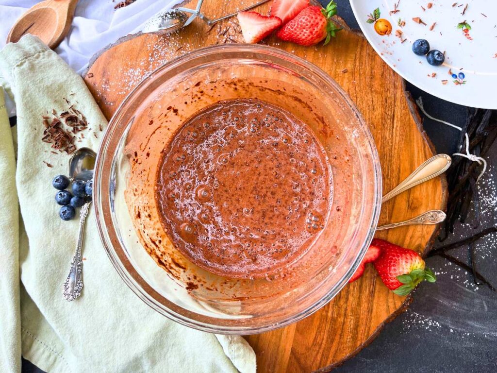 A glass bowl with chocolate crêpe batter inside.