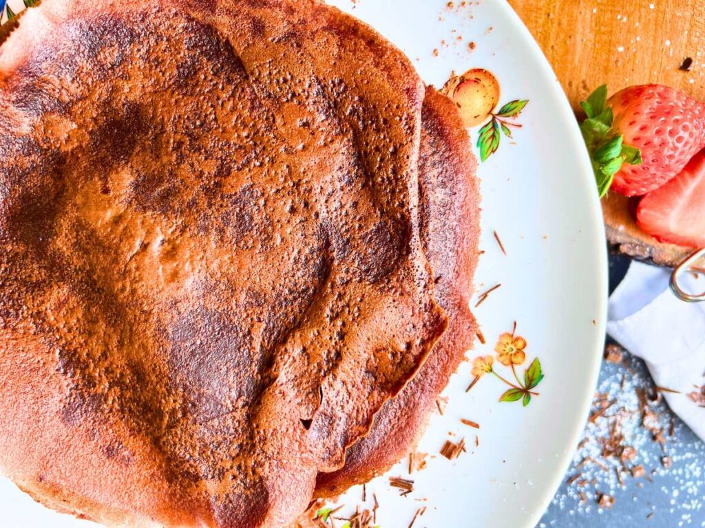 A stack of chocolate crêpes on a white cake plate.