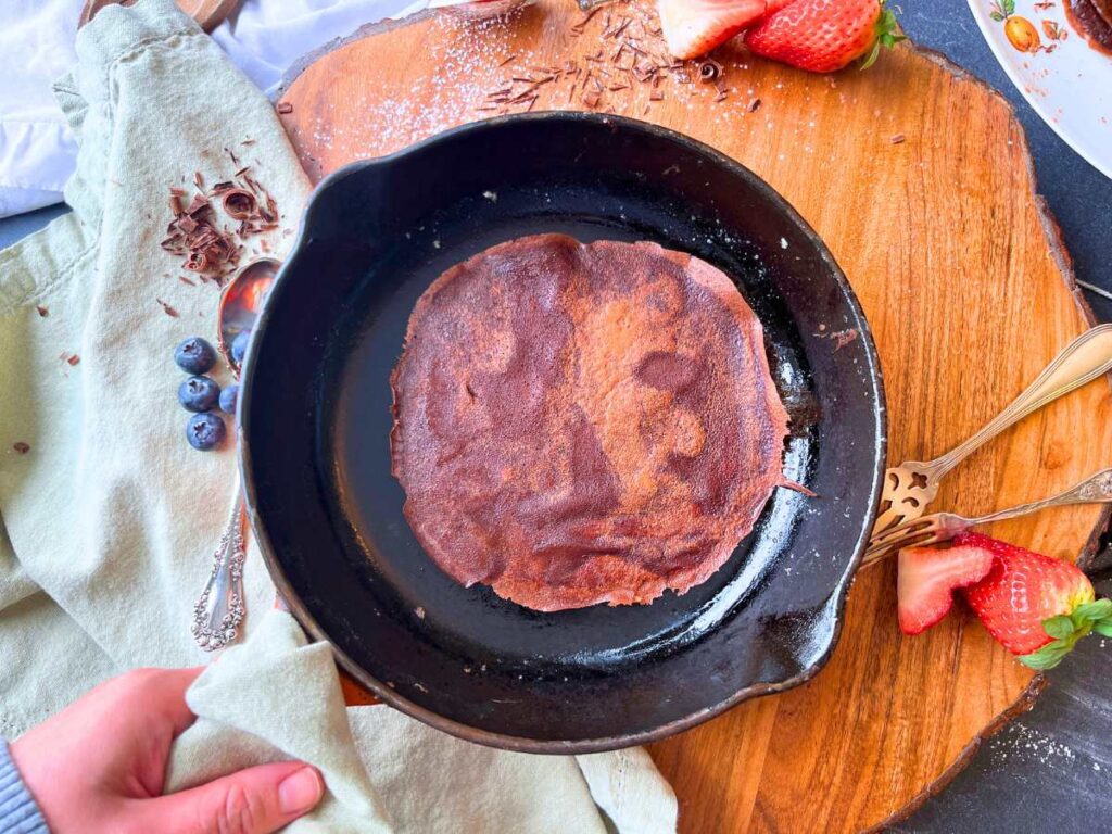 A cooked chocolate crêpe in a cast iron skillet.