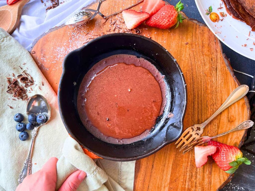 A cast iron skilled with chocolate crêpe batter cooking inside.