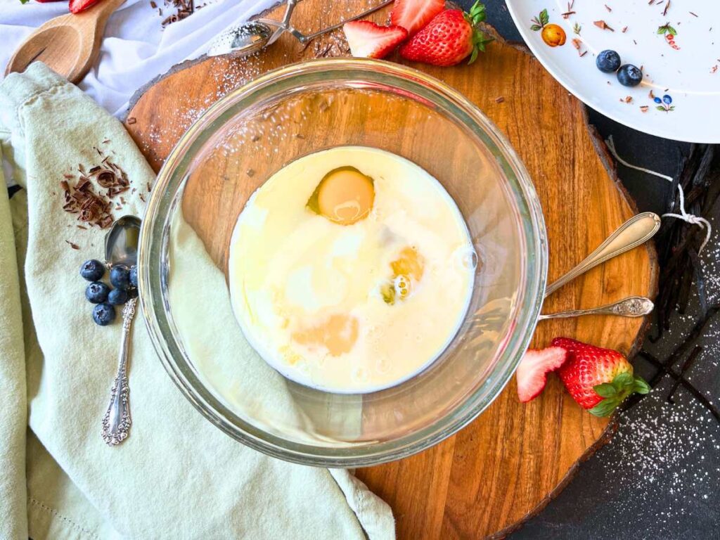 A glass bowl with milk and eggs inside.