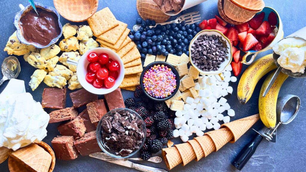 A table full of ice cream, toppings, sauces, and ice cream cones.