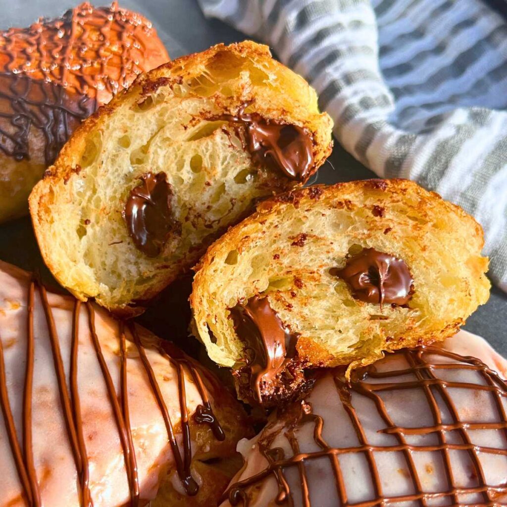 A group of iced chocolate croissants. Once is split in half.