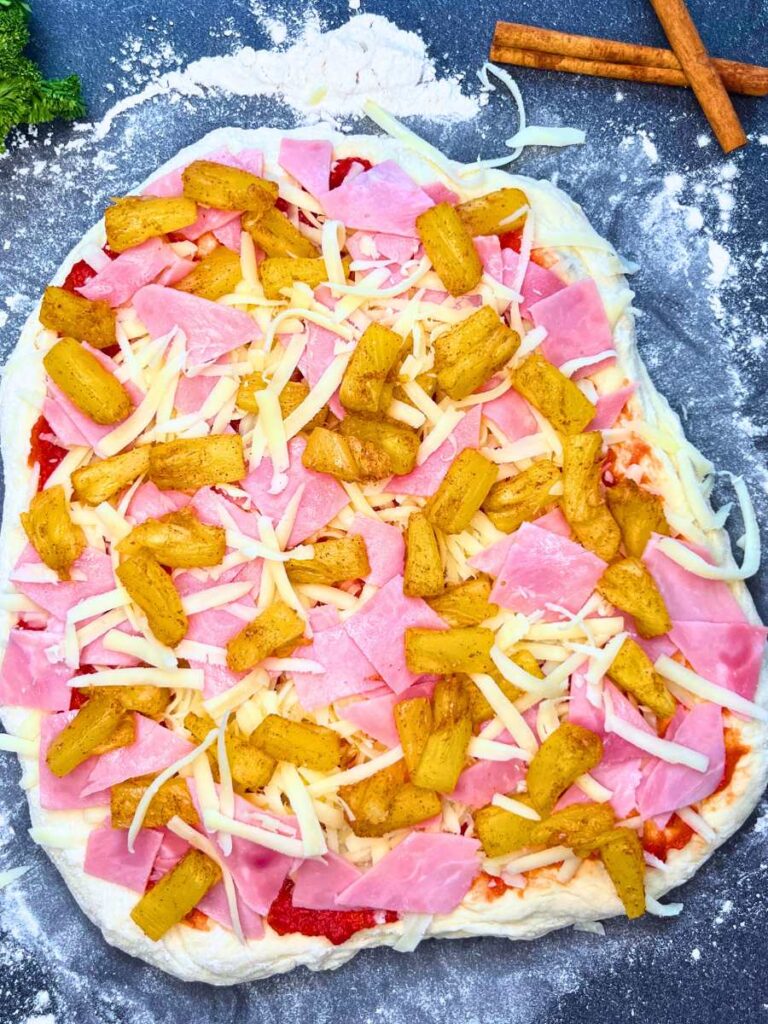 An unbaked pizza with ham and pineapple on top.