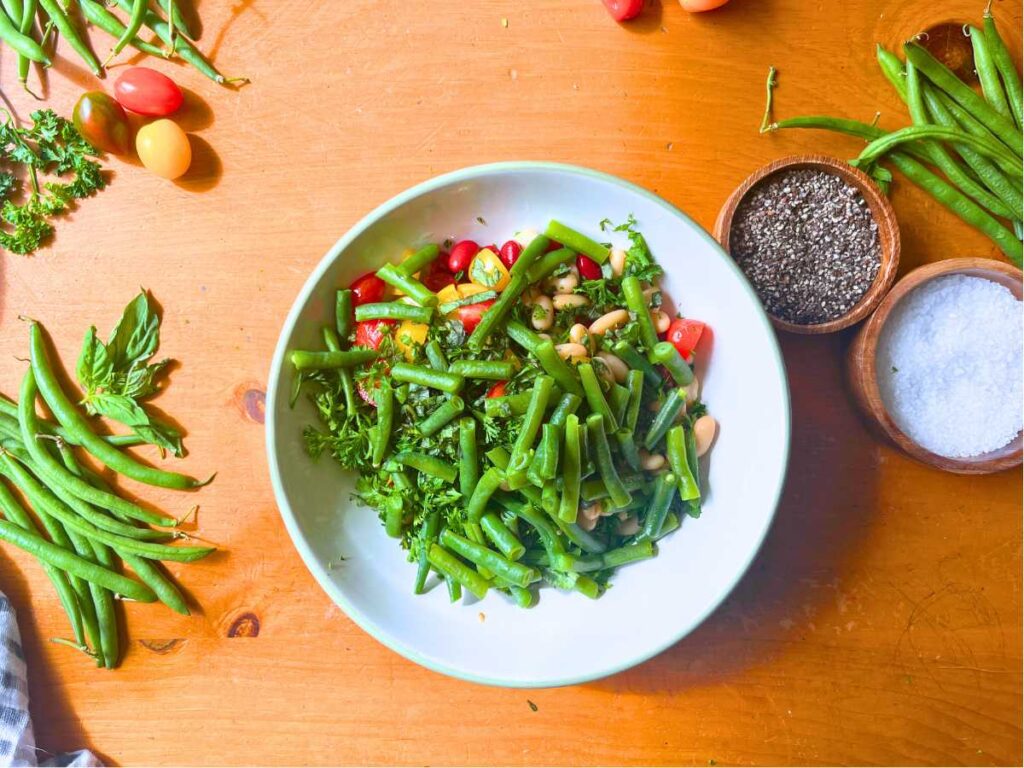 A large white bowl with green beans on top of sliced tomatoes.