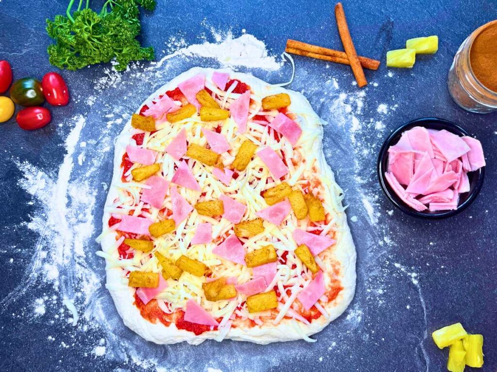 Pizza dough topped with ham and pineapple chunks.