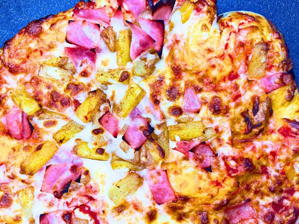 A baked pizza with ham and pineapple on top.
