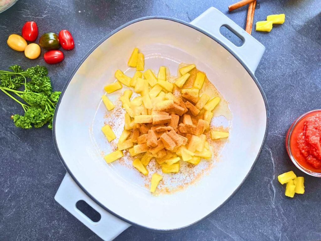 A sauce pot with pineapple chunks and cinnamon inside.