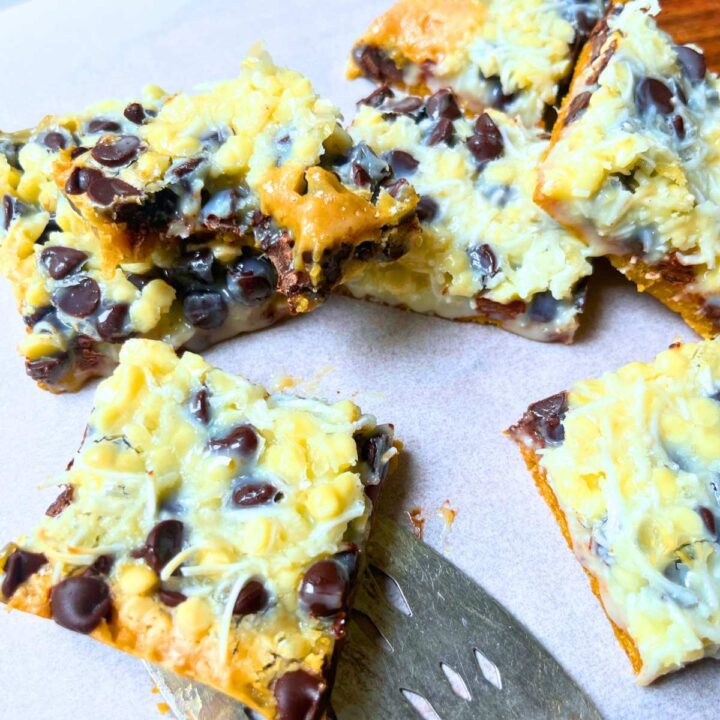 A group of hello Dolly squares on a piece of parchment paper. There is a serving spatula under one.