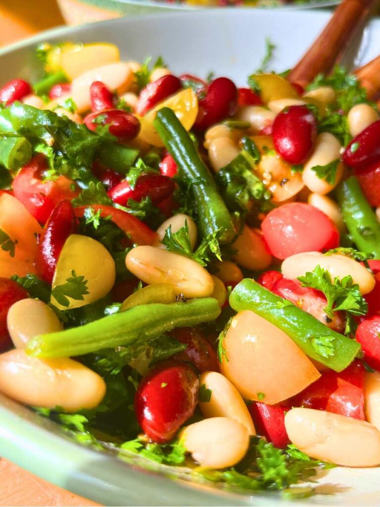 A side view of a bean and tomato salad in a white and green bowl.