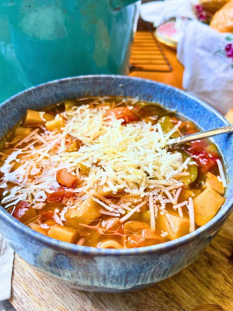 A blue bowl full of minestrone soup with grated cheese on top.
