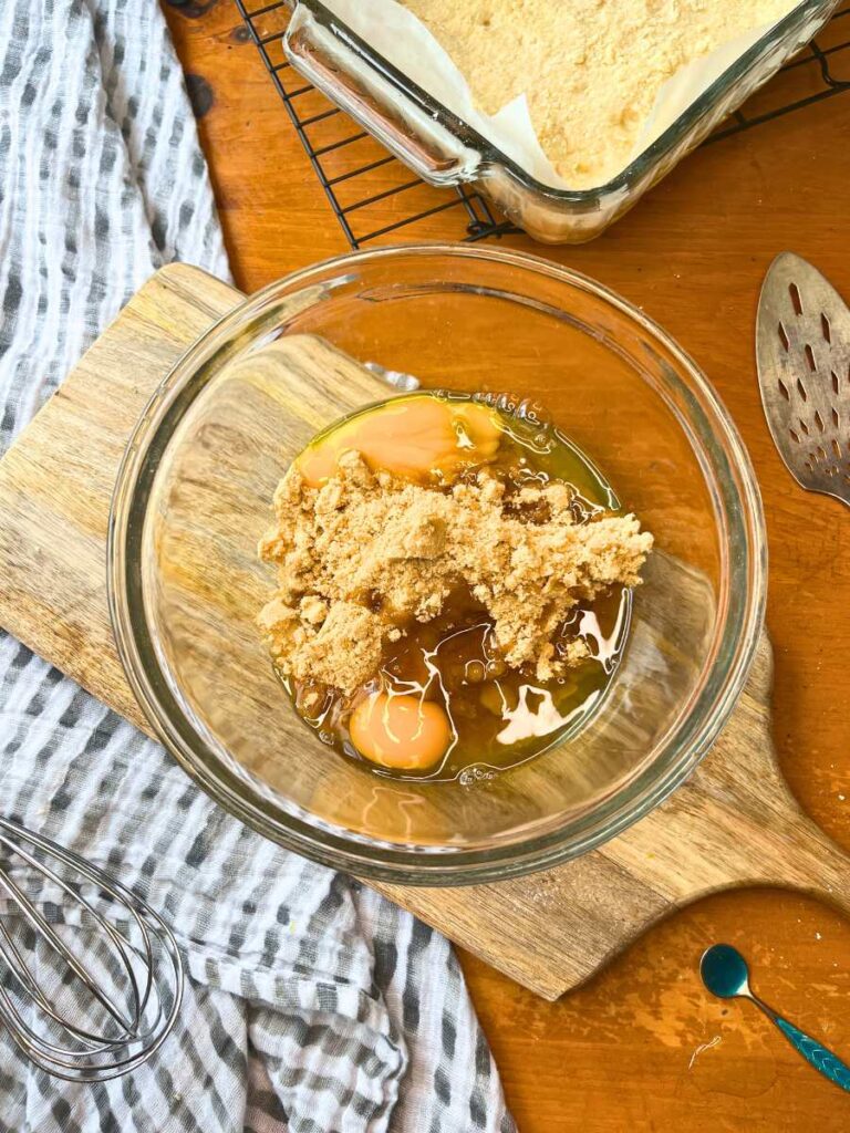 A large glass bowl with brown sugar and eggs inside.