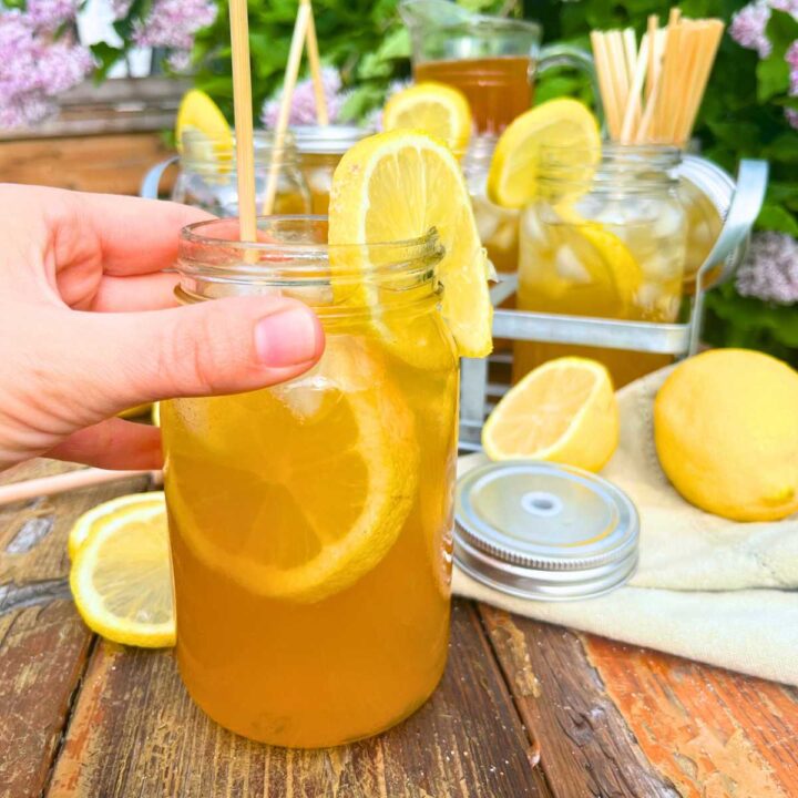 A woman is holding a glass jar cup filled with iced tea and sliced lemon.