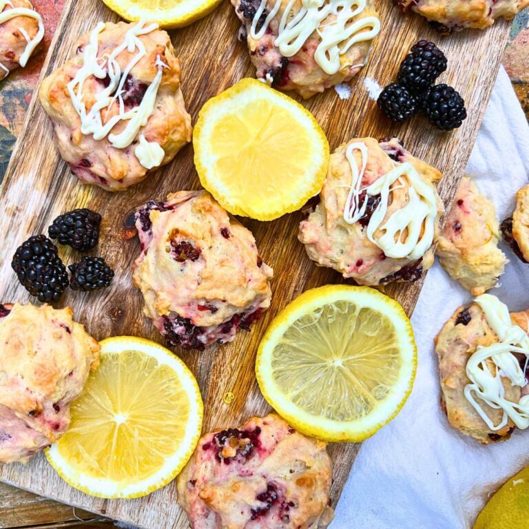 A wooden board filled with lemon and blackberry biscuits. There are lemon slices and fresh blackberries on the board.