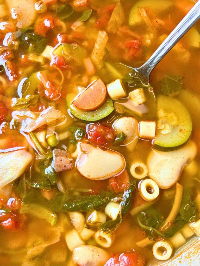 A close up look at minestrone soup in a large pot. There is a ladle inside.