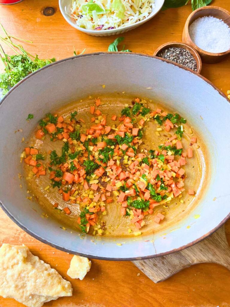 A Dutch oven with small diced carrots, celery, and shallots inside.
