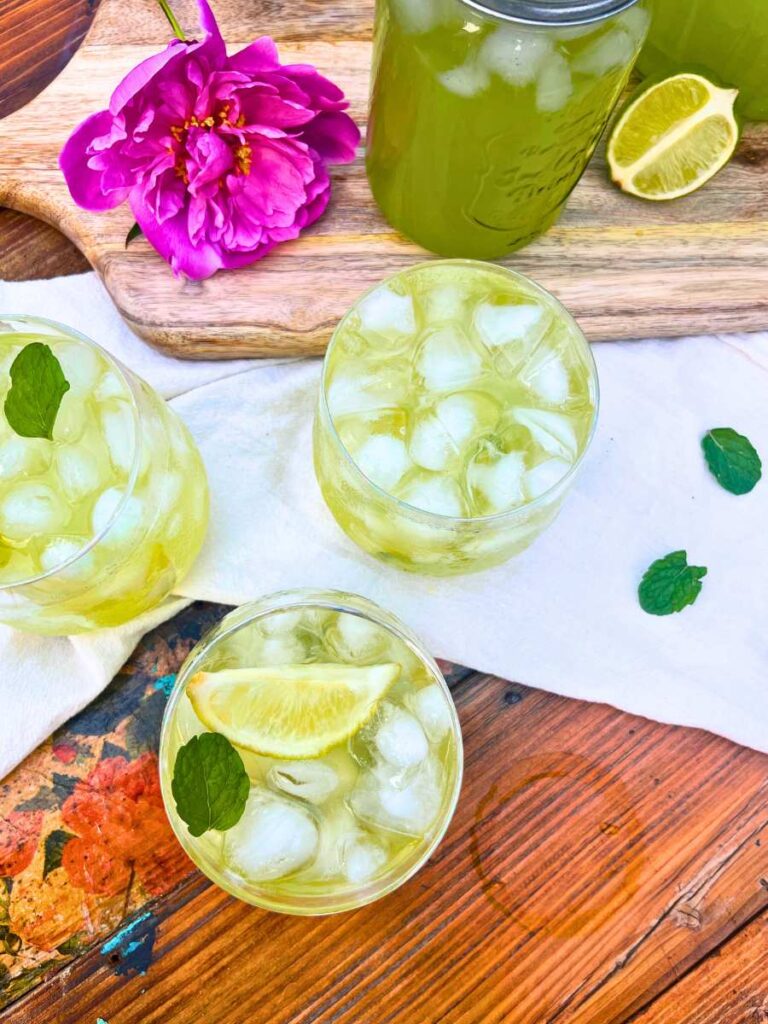 Three glasses of limeade with ice. There are lime wedges inside and mint leaves.