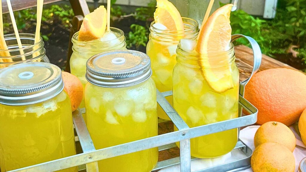 A tray with glass jars filled with ice, orangeade, and orange wedges.