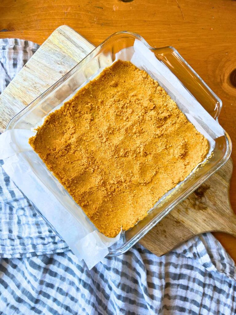 A graham cracker base in a parchment lined square glass pan.