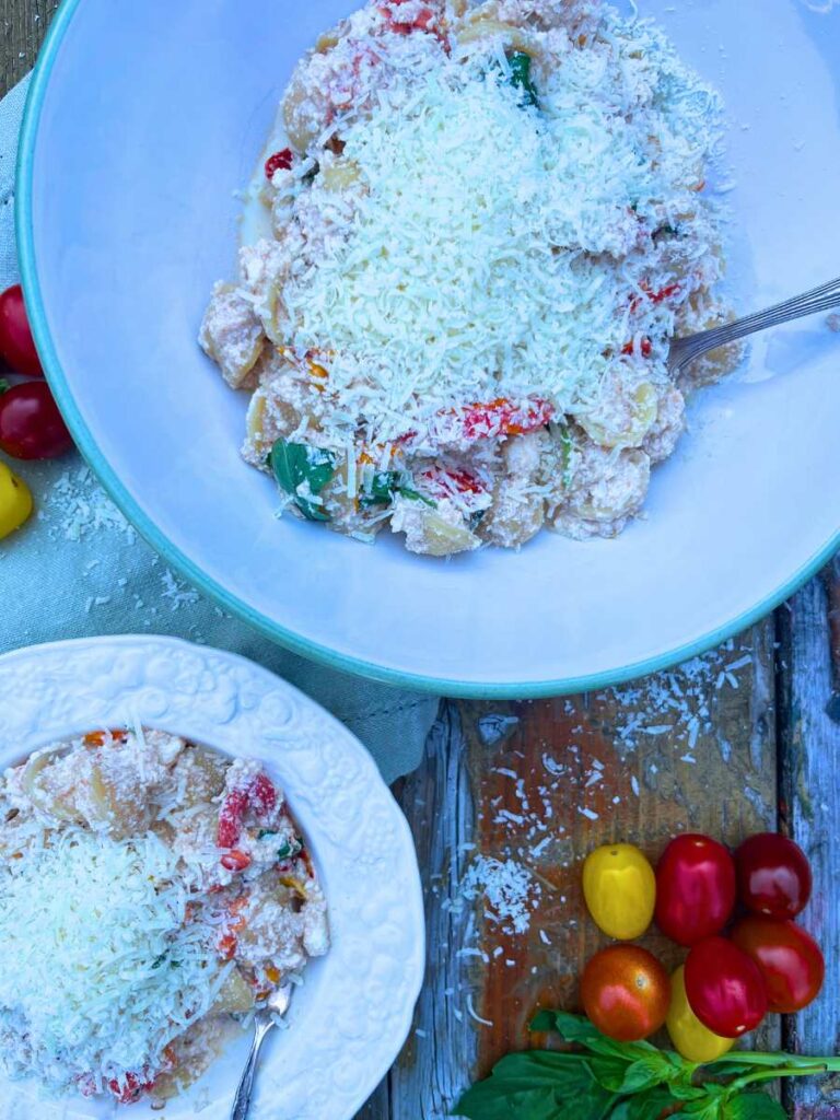 Two bowls of pasta with cooked tomato and basil. There is parmesan cheese on top.