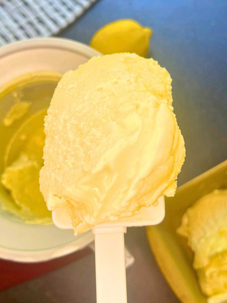 A woman is holding up a white spatula with lemon gelato.